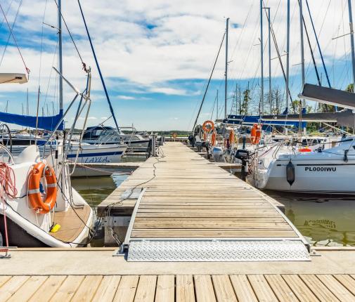 Nadbrzeże cumownicze oraz pomost z odnogami cumowniczymi y-boom. Po obu stronach przycumowane łodzie żaglowe 